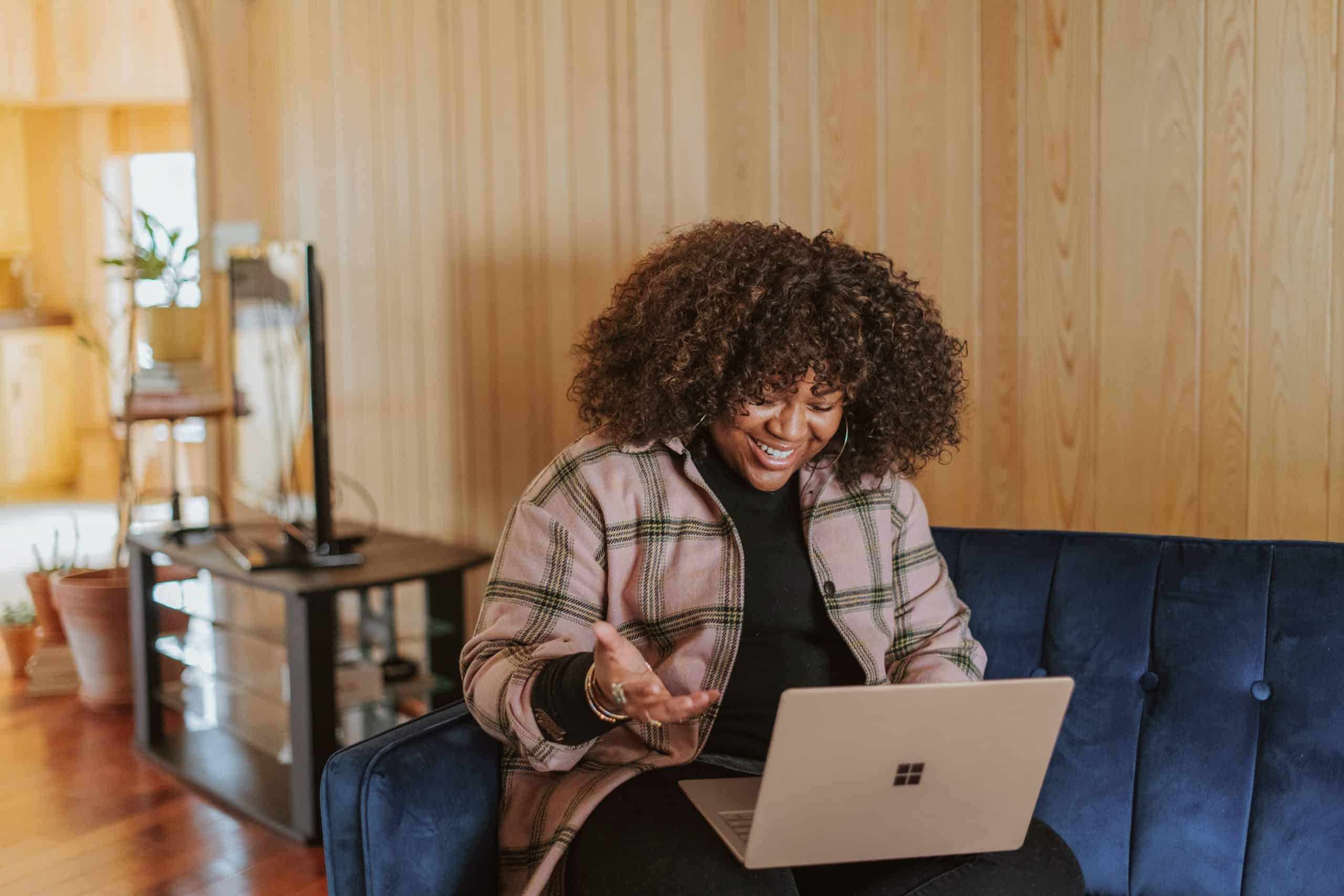Happy female smiling at laptop whilst sitting on a sofa.