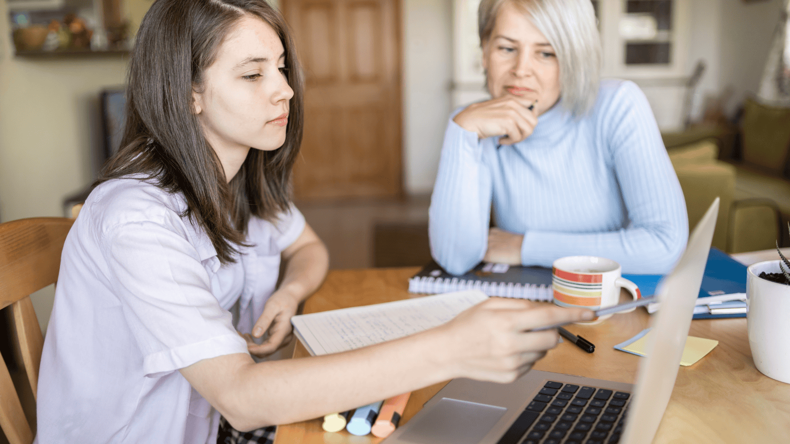 Mother supporting her daughter with her schooling, looking at information on a laptop.